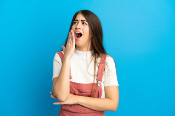 Young caucasian woman isolated on blue background yawning and covering wide open mouth with hand