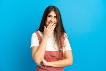 Young caucasian woman isolated on blue background happy and smiling covering mouth with hand