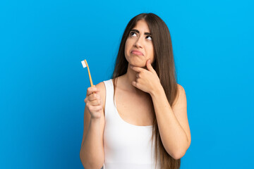 Young caucasian woman brushing teeth isolated on blue background and looking up