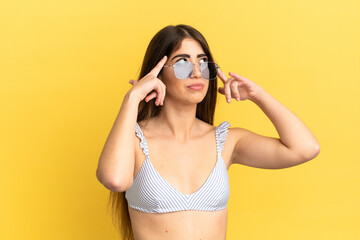 Young caucasian woman in swimsuit in summer holidays isolated on yellow background having doubts and thinking