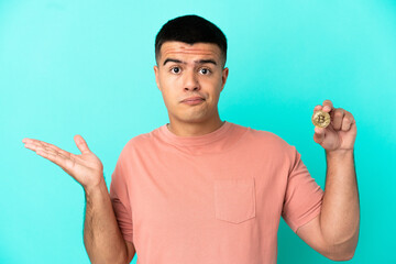 Young handsome man holding a Bitcoin over isolated blue background having doubts while raising hands