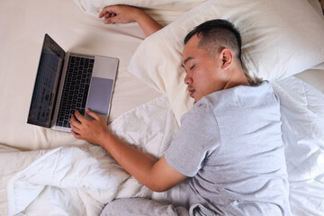 Top view of sleepy man working on laptop while sleeping on a bed