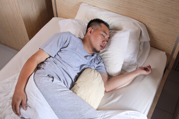 Fototapeta premium Young Asian man sleeping and snoring loudly lying in the bed