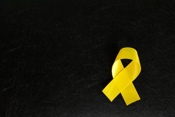 Yellow cancer awareness ribbon isolated on dark black background. Bone cancer awareness and suicide...