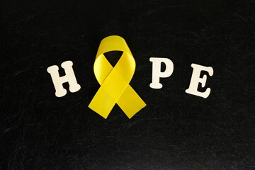 Yellow cancer awareness ribbon color with word hope on dark black background. Bone cancer awareness...