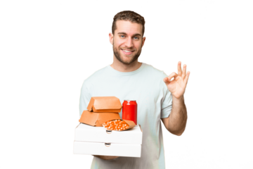 Young handsome blonde man holding pizzas and burgers over isolated background showing ok sign with fingers