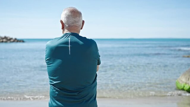 Senior grey-haired man standing backwards at seaside