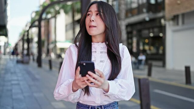 Young chinese woman using smartphone with serious expression at street