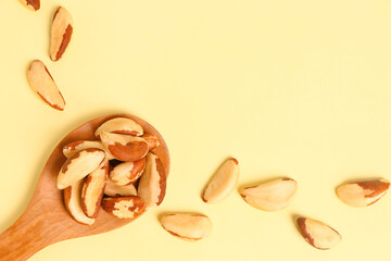 Wooden spoon of tasty Brazil nuts on yellow background