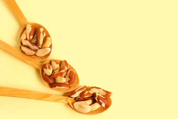Wooden spoons of tasty Brazil nuts on yellow background, closeup