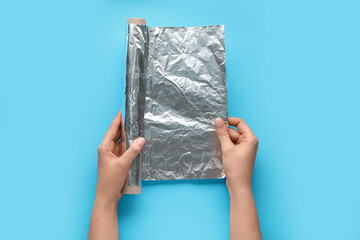 Female hands with roll of aluminium foil on color background