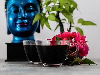 Low angle shot  of black coffee, flowers with defocused tree and buddha face.