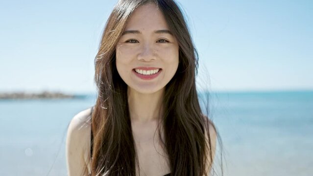 Young chinese woman tourist wearing swimsuit blowing kiss at seaside
