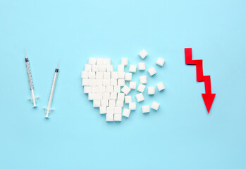 Heart made of sugar with syringes for insulin injection and arrow directed downwards on blue background