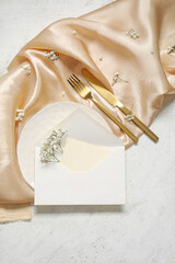 Clean plate with blank invitation card, cutlery and gypsophila flowers on white table
