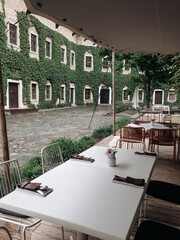 Restaurant terrace under a canopy in a cozy courtyard with a green wall