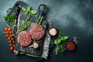 Obraz na płótnie Canvas Raw veal burger cutlet with spices and herbs. Ready to cook. On a dark stone background. Top view.