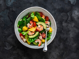 Delicious avocado, mango, shrimp, tomato salad  on a dark background, top view
