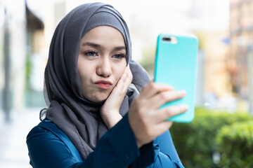 Happy young Muslim woman using smartphone for taking selfie photo app and upload