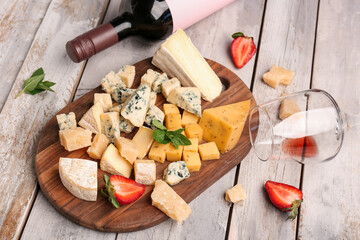 Pieces of tasty cheese, glass and bottle with wine on light wooden background