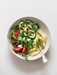 Vegetarian lunch - pasta and grilled zucchini, tomatoes, arugula, feta salad on a light background, top view