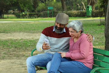 Mid aged couple sitting on the bench in a lush green serene environment having a good time together. They are happily enjoying their time. smiles all around.