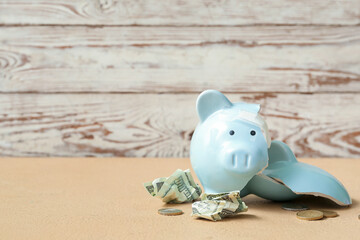 Broken patched piggy bank with money on table near wooden wall. Concept of bankruptcy