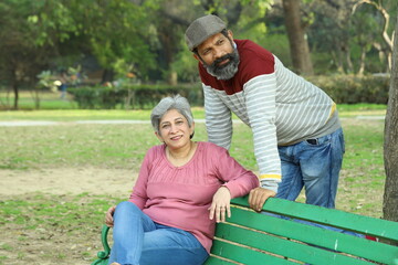 Mid aged couple sitting on the bench in a lush green serene environment having a good time together. They are happily enjoying their time. smiles all around.