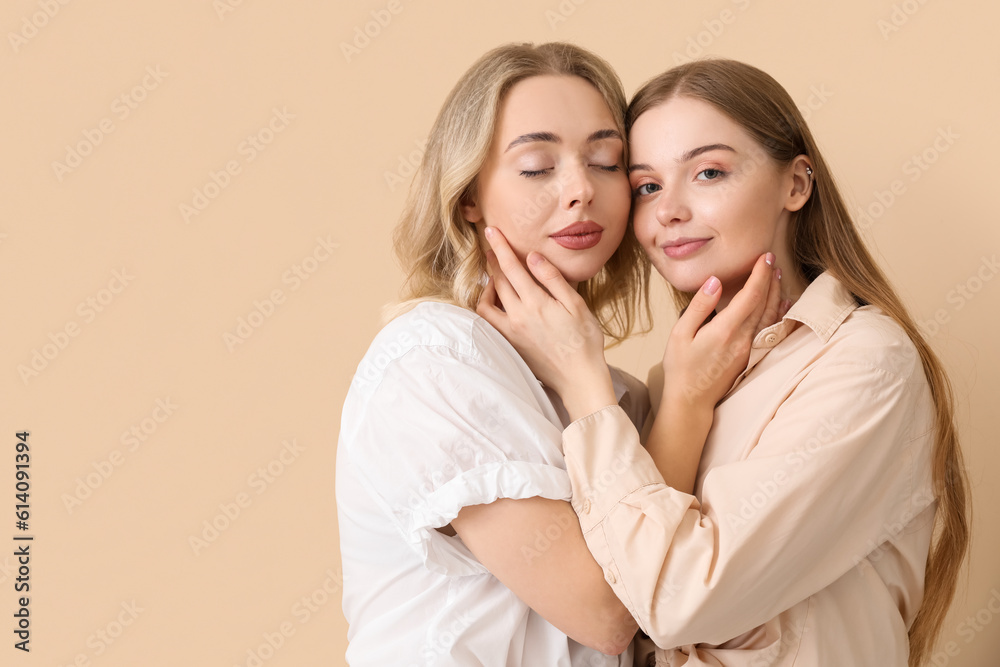 Wall mural Young sisters hugging on beige background