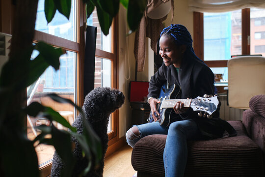 African Woman Playing The Guitar Next To A Dog At Home