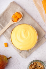 Bowl of tasty cheddar sauce and spoon with cheese cubes on white grunge background