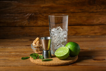 Glass with ice, measure cup and ingredients for preparing mojito on wooden background
