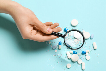 Female hand with magnifier and pills on blue background