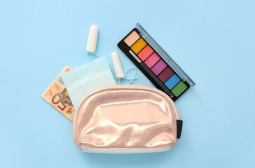 Lady's cosmetic bag with menstrual pads, tampons, money and eyeshadows on blue background