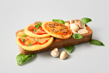 Board with different tasty mini pizzas on grey background