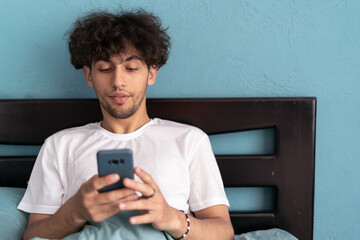 Fototapeta premium Handsome man, bed and phone in home bedroom for social media, internet browsing in the morning. Technology, relax and networking at home