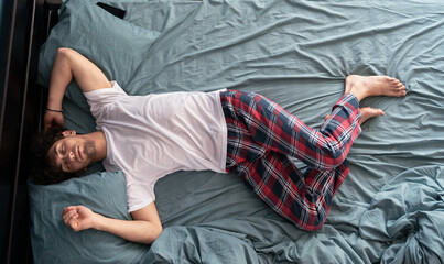 Top view of young arab guy in pajamas resting at home, sleeping on his back in comfortable bed, full length shot. Healthy sleeping concept.