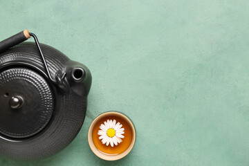 Teapot with cup of natural chamomile tea and flower on green grunge background