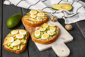 Tasty toasts with quail eggs, avocado and cucumber on dark wooden background