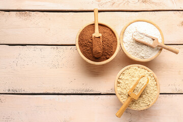 Wooden bowls with different types of flour and cacao on light wooden background