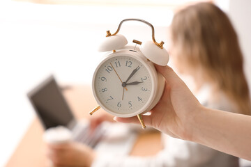 Woman with alarm clock in office, closeup