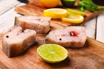 Board with pieces of raw codfish with lime on light wooden background