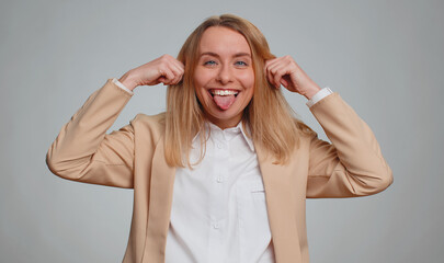 Portrait of young businesswoman making playful silly facial expressions and grimacing, fooling around, showing tongue. Female girl in formal suit. Pretty woman isolated on gray studio background
