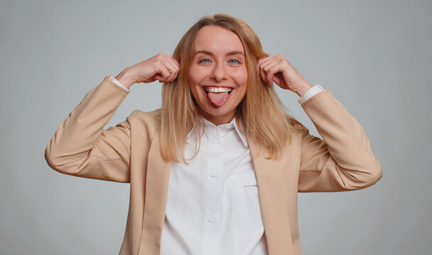 Portrait of young businesswoman making playful silly facial expressions and grimacing, fooling around, showing tongue. Female girl in formal suit. Pretty woman isolated on gray studio background