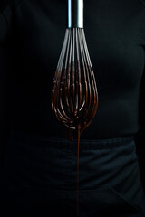 Kitchen metal whisk in chocolate. Kitchen utensils. On a black background.