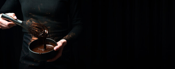 Preparation of melted chocolate in the hands of a chocolatier. Kitchen whisk. On a black background.