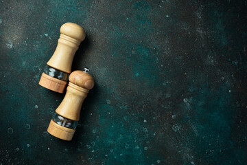 Wooden pepper and salt mill. On a dark green-turquoise background. Free space for text.