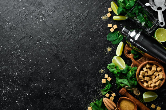 Mojito preparation: shaker, lime, mint and ice. On a black stone background. Top view.