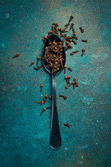 Fragrant cloves in a metal spoon. Spices and condiments. Top view. On a dark textured background.