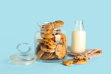 Jar with cookies, bottle of milk and towel on blue background